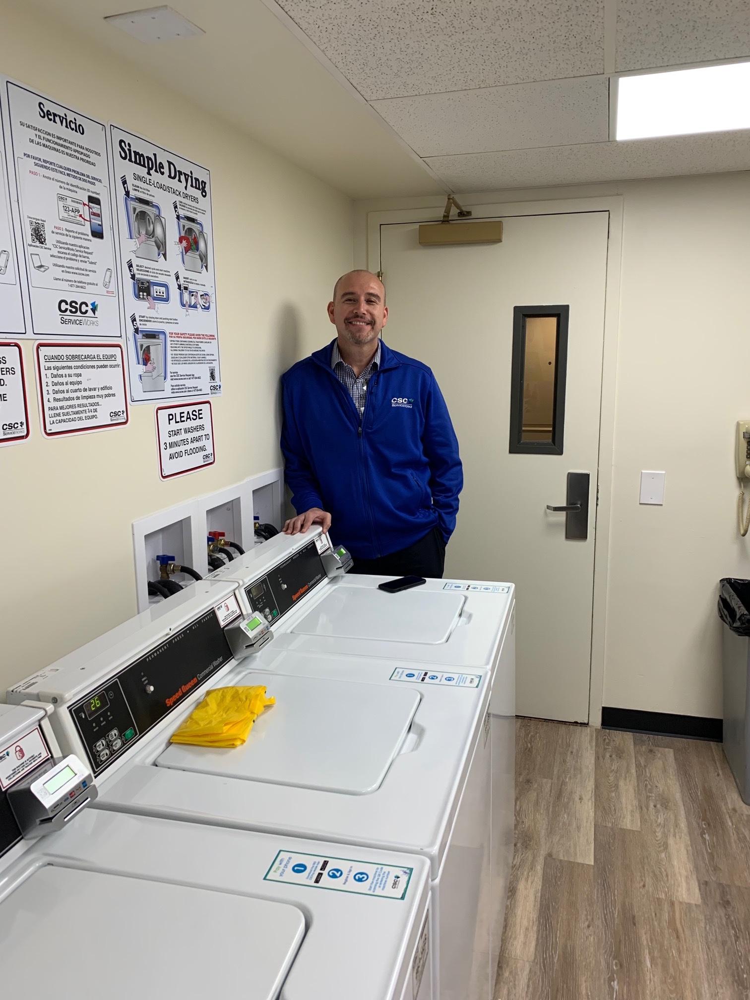 CSC ServiceWorks employee smiling and standing near a laundry machine