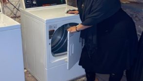 woman smiling and standing by a laundry machine